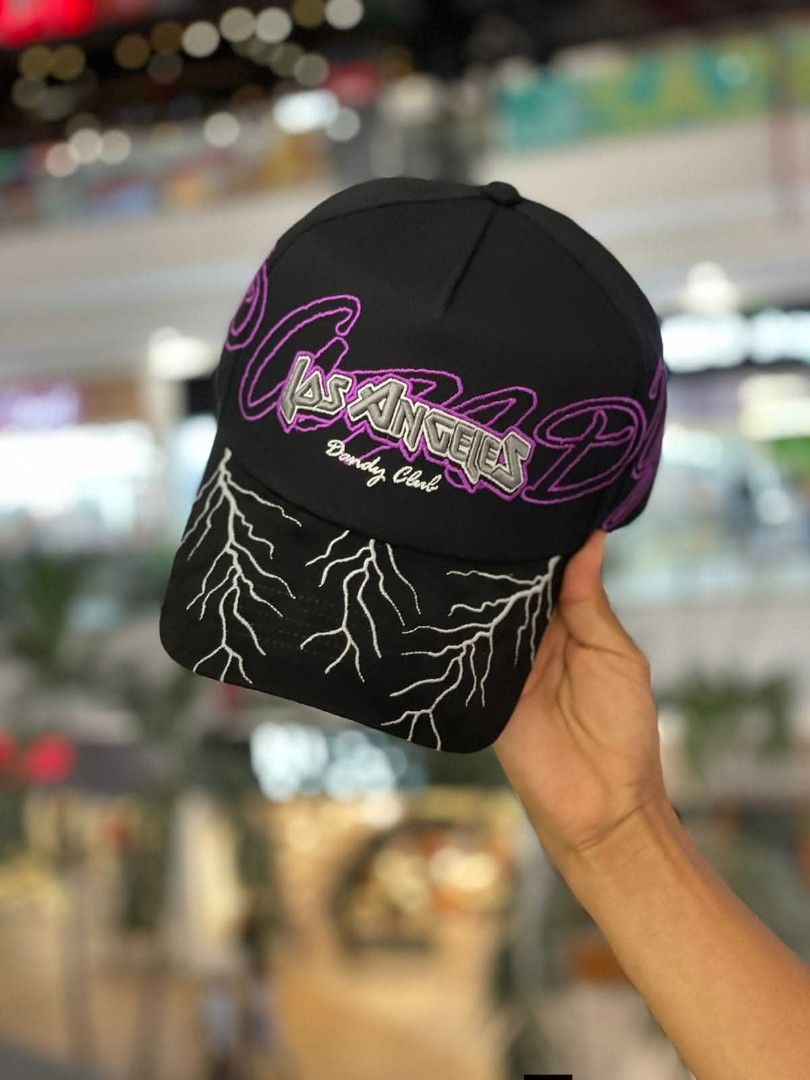Dandy Hats Los Angeles Lightning Cap Black Purple (Category: Caps & Hats) located in Dipolog. Submitted by just_thriftfinds (Listing ID 1471060423, Image 2). Description: Black baseball cap from Dandy Hats. Los Angeles lettering embroidered across the front with purple outline and Dandy Club text. Brim features white lightning bolt embroidery. Purple inner lining with printed branding throughout and branded taping. Adjustable strap in the back..