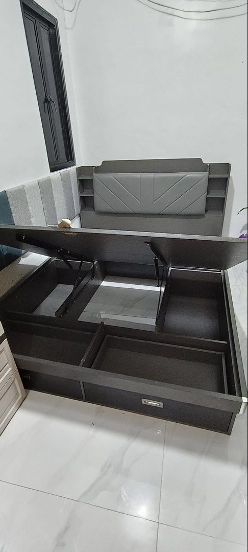 Dark Grey Storage Bed Frame with Headboard and Drawers (Category: Bed Frames & Mattresses) located in Calamba. Submitted by missarc (Listing ID 1471067546, Image 3). Description: Dark grey wooden bed frame featuring hydraulic lift storage underneath. Headboard built with upholstered padded cushion and side shelving compartments. Two pull-out drawers integrated at the foot of the base. Clean dark wood finish throughout. Mattress not included..