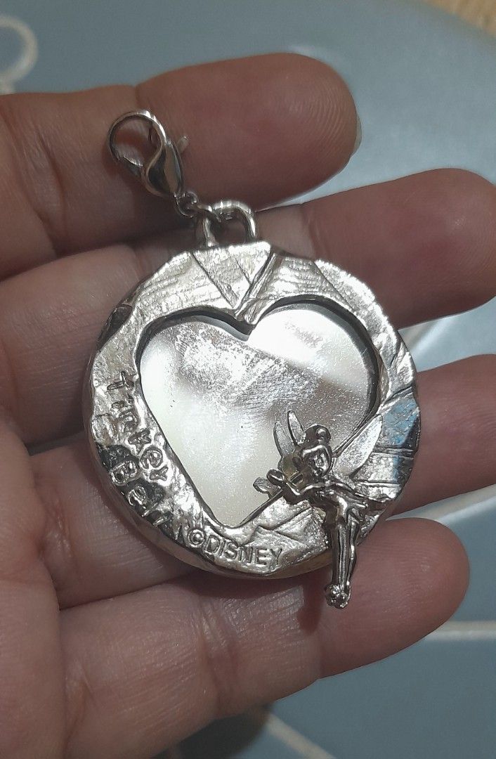 Disney Tinker Bell Heart Charm Keychain (Category: Charms) located in Bocaue. Submitted by marajapansurplus (Listing ID 1470979378, Image 2). Description: - Official Disney Tinker Bell charm - Silver-tone metal with heart-shaped frame - Features engraved Tinker Bell signature and copyright stamp - Reverse side has a fun star and silhouette graphic - Equipped with a sturdy lobster clasp - Perfect for clipping onto bags, keys, or pouches.
