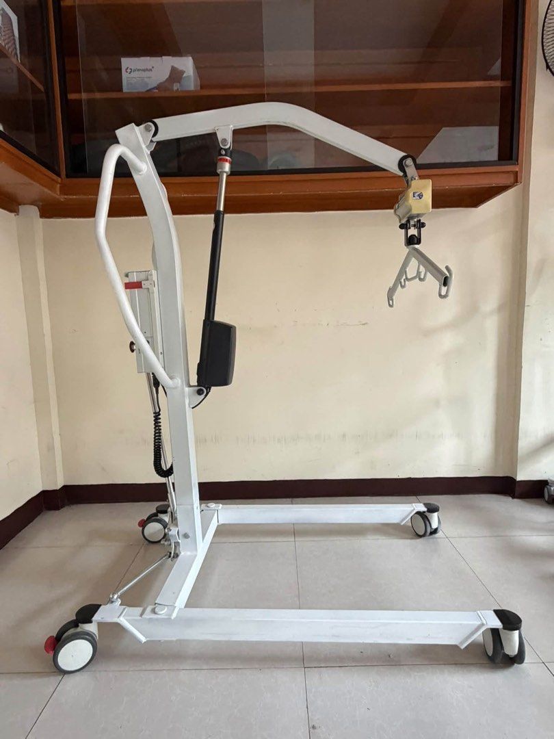 Electric Patient Lift Transfer Machine with Sling (Category: Medical Supplies & Tools) located in Manila. Submitted by calmdolphin.87b0e4 (Listing ID 1470957973, Image 2). Description: - Electric patient lift for smooth bed-to-wheelchair transfers - Sturdy white metal frame with rolling, lockable casters - Rechargeable battery pack with convenient handheld controller - Includes green support sling as shown in photos - Manual leg width adjustment 