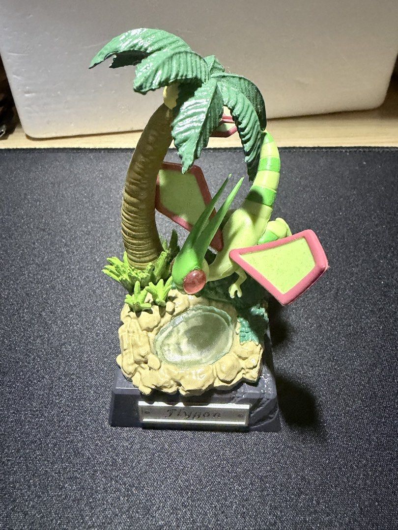 Flygon figure diorama with palm tree base (Category: Figurines & Statues) located in Mandaluyong City. Submitted by juliansthings (Listing ID 1471089672, Image 1). Description: Flygon collectible figure perched over a small pool next to a palm tree. Detailed diorama base includes rocks and foliage. Nameplate attached to the front of the dark grey stand. Green and pink color scheme on the Pokemon. Good display piece for fans. Buyer shoulders SF Bo