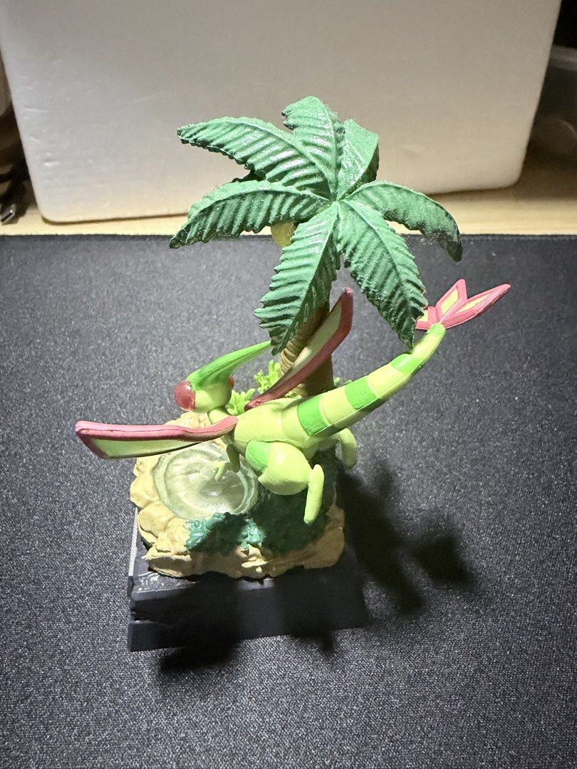 Flygon figure diorama with palm tree base (Category: Figurines & Statues) located in Mandaluyong City. Submitted by juliansthings (Listing ID 1471089672, Image 3). Description: Flygon collectible figure perched over a small pool next to a palm tree. Detailed diorama base includes rocks and foliage. Nameplate attached to the front of the dark grey stand. Green and pink color scheme on the Pokemon. Good display piece for fans. Buyer shoulders SF Bo