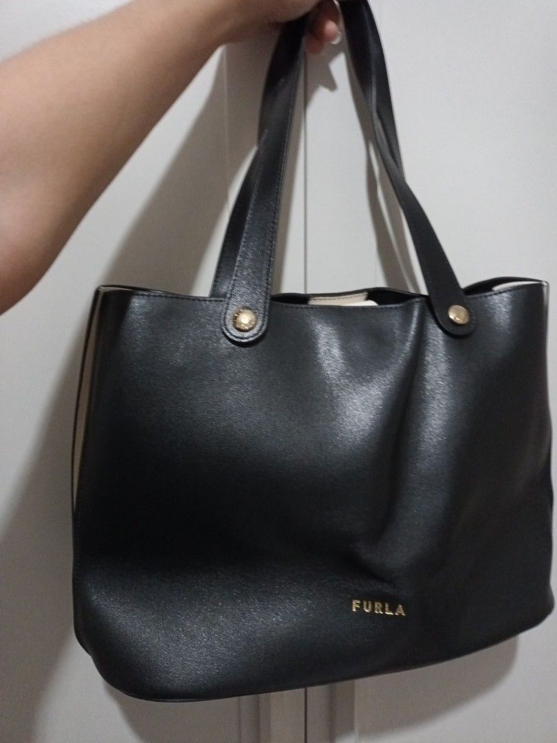 Furla Black Leather Tote Bag (Category: Luxury Bags & Wallets) located in Quezon. Submitted by ja8720 (Listing ID 1471052569, Image 2). Description: - Authentic Furla black leather tote bag with elegant gold-tone hardware - Open top design with a secure snap button tab closure - Dual shoulder straps accented with branded gold buttons - Convenient exterior slip pocket at the back - Includes a removable white zip pouch featuring the Furla Genuine L