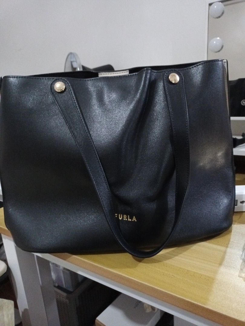 Furla Black Leather Tote Bag (Category: Luxury Bags & Wallets) located in Quezon. Submitted by ja8720 (Listing ID 1471052569, Image 1). Description: - Authentic Furla black leather tote bag with elegant gold-tone hardware - Open top design with a secure snap button tab closure - Dual shoulder straps accented with branded gold buttons - Convenient exterior slip pocket at the back - Includes a removable white zip pouch featuring the Furla Genuine L