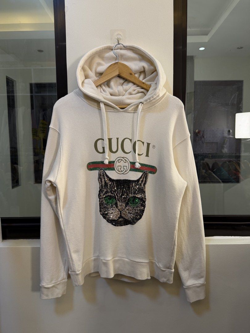 Gucci Pullover Hooded Sweatshirt (Category: Coats, Jackets and Outerwear) located in Paranaque City. Submitted by preluxeshop_ph (Listing ID 1471015198, Image 2). Description: Brand: Gucci •Style: Pullover Hooded Sweatshirt / Hoodie •Color: Off-White / Cream •Design Features: Front embroidered sequin cat face graphic, signature green-and-red Web stripe accent, bold “GUCCI” logo lettering, attached drawstring hood, and ribbed cuffs and hem •Made I