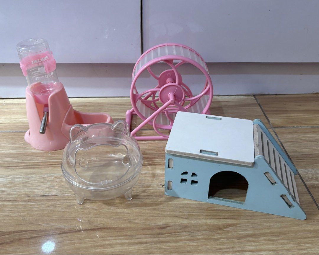 Hamster cage accessories bundle house wheel water bottle (Category: Homes & Other Pet Accessories) located in Quezon City. Submitted by kyjnll (Listing ID 1470987940, Image 1). Description: - Bundle of 4 essential hamster accessories - Blue & white wooden hideout house with climbing ramp - Pink silent running wheel for quiet nighttime exercise - Pink water bottle with integrated food dish base - Clear plastic cat-eared container for sand bath - C