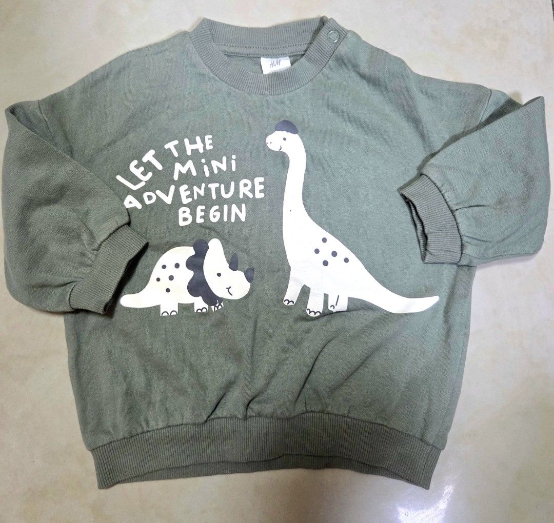 H&M Green Dinosaur Sweatshirt 6-9M (Category: Babies & Kids Fashion) located in Manila. Submitted by allthings.wellloved (Listing ID 1470963763, Image 1). Description: - Brand: H&M - Design: Sage green with cute dinosaurs and "Let the mini adventure begin" text - Size: EUR 74 / US 9M - Features: Convenient shoulder snap buttons for easy dressing, ribbed neckline, cuffs, and hem - Material: Super soft cotton blend inside and out - Condition: Excel