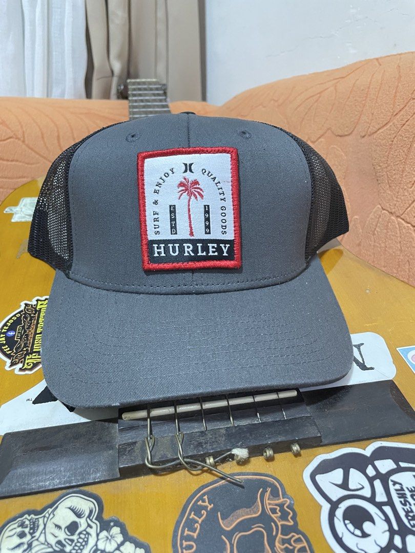 Hurley Trucker Cap Grey Snapback Hat (Category: Caps & Hats) located in Manila. Submitted by clementdav22513 (Listing ID 1471026099, Image 1). Description: - Brand: Hurley (The Classics / Yupoong line) - Color: Grey front with black mesh back - Design: Red and white 'Surf & Enjoy Quality Goods Estd 1999' palm tree front patch - Material: 100% polyester, breathable mesh design - Closure: Adjustable snapback with Hurley logo detail - Condition: Bra