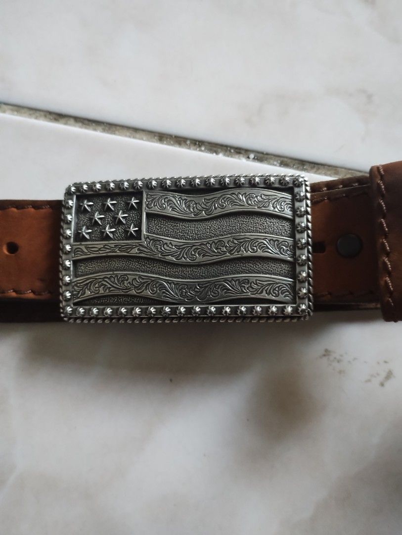Leather Belt With American Flag Buckle (Category: Belts) located in Imus. Submitted by darylg88358770 (Listing ID 1471023278, Image 3). Description: - Style: Classic Western style - Strap: Genuine brown leather with sturdy edge stitching - Buckle: Silver-tone metal plate featuring an embossed American flag, stars, and floral scroll patterns - Closure: Standard pin buckle on the back - the items trifted fresh from bale size 34 .