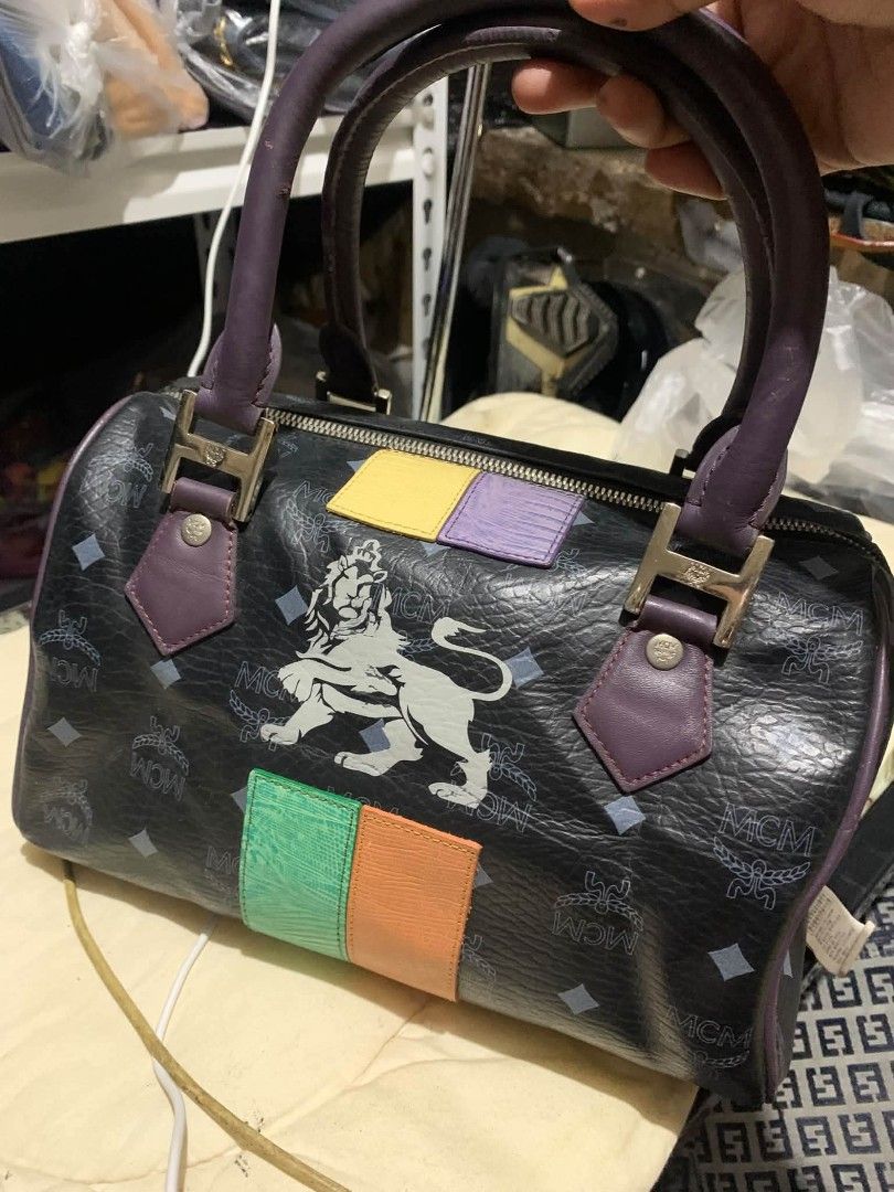 MCM Black Monogram Lion Boston Bag (Category: Luxury Bags & Wallets) located in Daraga. Submitted by thethriftcity2024 (Listing ID 1470981221, Image 2). Description: - Black MCM Boston bag with classic monogram print - Features a bold, large white lion graphic on the side - Dual purple leather top handles and vibrant leather patches in yellow, purple, green, and orange - Secure top zip closure with dual pullers and a contrast green pull tab - Cre