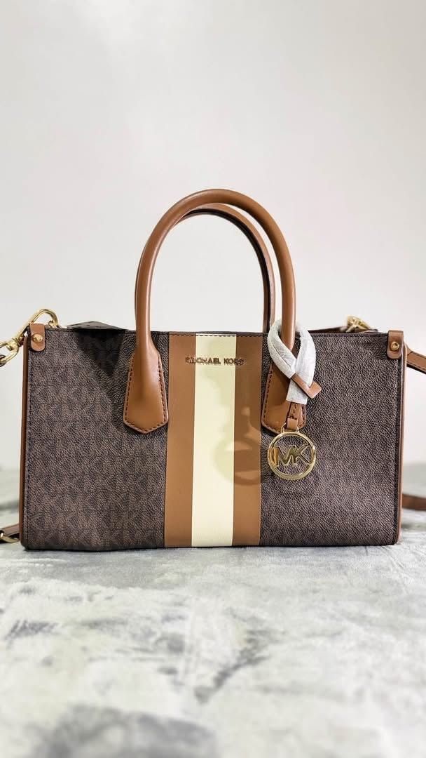Michael Kors Brown Monogram Satchel Bag With Stripe (Category: Luxury Bags & Wallets) located in Las Pinas. Submitted by raebelran (Listing ID 1471037686, Image 1). Description: - Brand: Michael Kors - Design: Signature brown monogram with brown/cream vertical stripes - Hardware & Logo: Gold foil logo lettering and hanging circular MK charm - Condition: Brand new with protective wrapping intact on the handle and charm - Straps: Double top handles