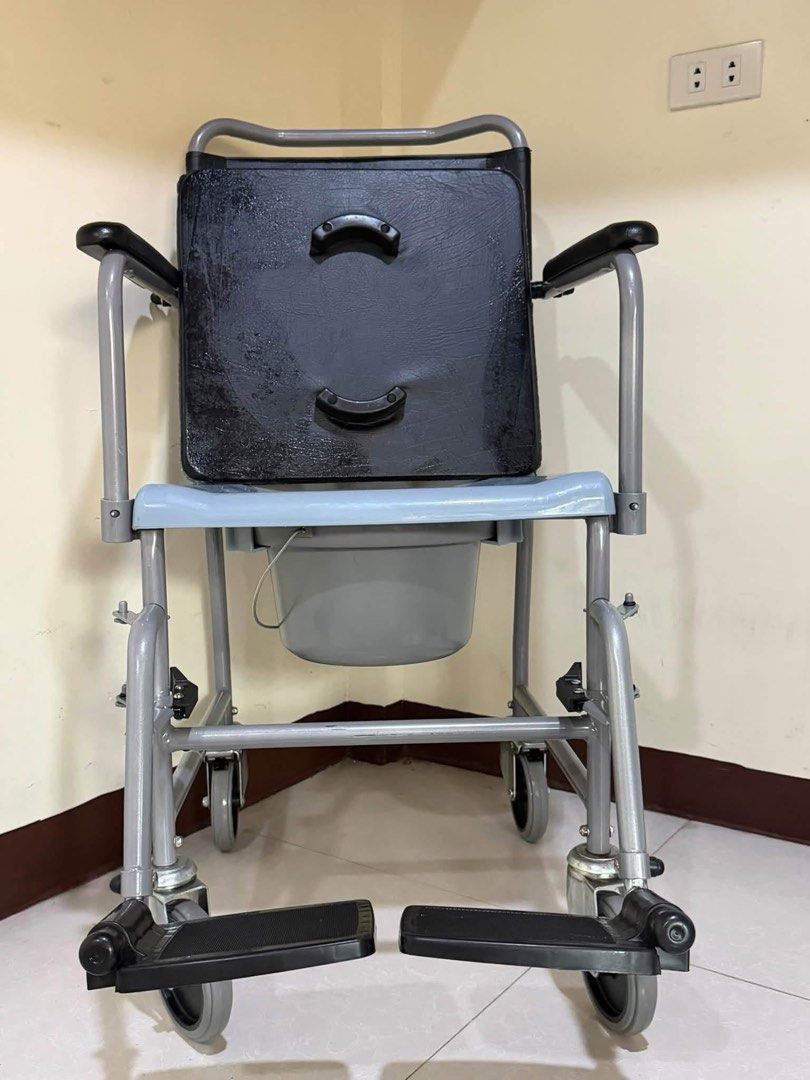 Mobile Commode Wheelchair with Detachable Bucket (Category: Wheelchairs) located in Manila. Submitted by calmdolphin.87b0e4 (Listing ID 1470955394, Image 3). Description: - Durable grey steel frame designed for elderly care and home mobility - Comfortable padded black backrest and seat cushion - Convenient removable commode bucket with lid and blue plastic toilet seat - Four locking caster wheels for safety and easy movement - Foldable footrests 