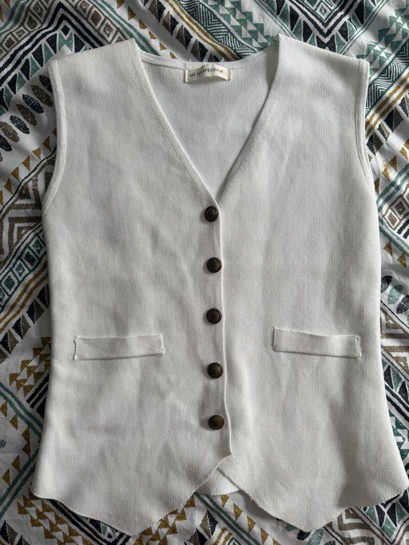 Mt. Matinee Basic White Knit Vest with Buttons (Category: Sleeveless) located in Manila. Submitted by decluterthings888 (Listing ID 1471077843, Image 1). Description: - Brand: Mt. Matinee Basic - Color: Clean, bright white - Style: V-neck, sleeveless knit vest with a soft texture - Details: Five dark brown contrast buttons and two small lower-waist front pockets - Hem: Unique downward-pointing scalloped hemline - Versatility: Great layering piece