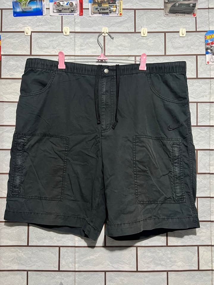 Nike The Athletic Dept. Cargo Shorts (Category: Shorts) located in Cagayan de Oro. Submitted by thrift4all (Listing ID 1471003476, Image 1). Description: - Brand: Nike (The Athletic Dept.) - Size: XL - Color: Black - Material & Fit: Elastic waistband with adjustable drawstring closure - Storage: Multiple functional cargo pockets on the sides - Details: Embroidered Nike swoosh near the left pocket and button detail on the front cargo flap - Condit