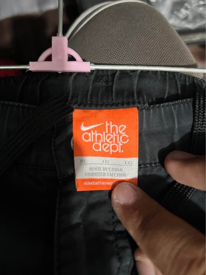 Nike The Athletic Dept. Cargo Shorts (Category: Shorts) located in Cagayan de Oro. Submitted by thrift4all (Listing ID 1471003476, Image 3). Description: - Brand: Nike (The Athletic Dept.) - Size: XL - Color: Black - Material & Fit: Elastic waistband with adjustable drawstring closure - Storage: Multiple functional cargo pockets on the sides - Details: Embroidered Nike swoosh near the left pocket and button detail on the front cargo flap - Condit