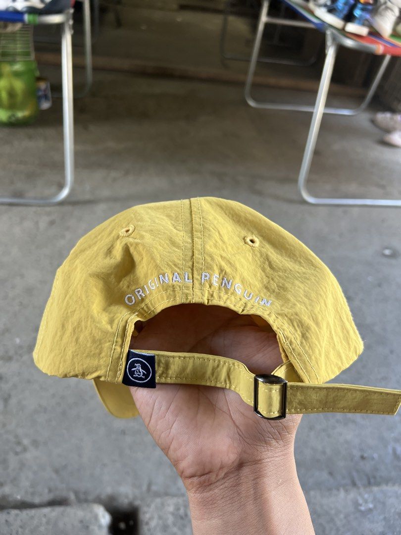 Original Penguin Yellow Nylon Baseball Cap (Category: Caps & Hats) located in Butuan. Submitted by nikthrift. (Listing ID 1470989710, Image 2). Description: - Brand: Original Penguin by Munsingwear - Color: Bright yellow - Material: 100% nylon - Details: Rubber penguin logo patch on front, embroidered lettering on back - Fit: Adjustable strap with metal buckle closure - Condition: Clean, well-maintained.