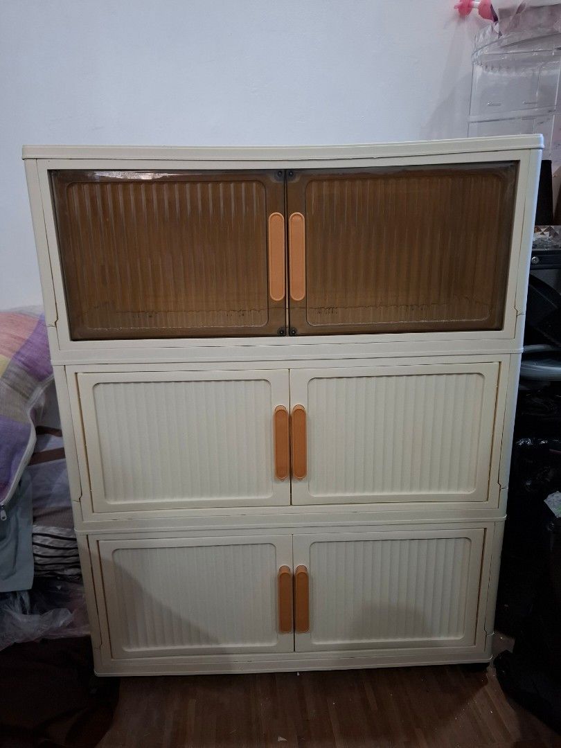 Plastic storage cabinet with multi-tier doors (Category: Shelves, Cabinets & Racks) located in Taguig. Submitted by cessyago123 (Listing ID 1470991537, Image 1). Description: - Multi-tier plastic storage cabinet for organizing household items - Features double doors with unique orange handles and cream-colored panel doors - Sturdy and durable construction with ample internal space - Doors open fully for easy access to all shelves - Versatile neut
