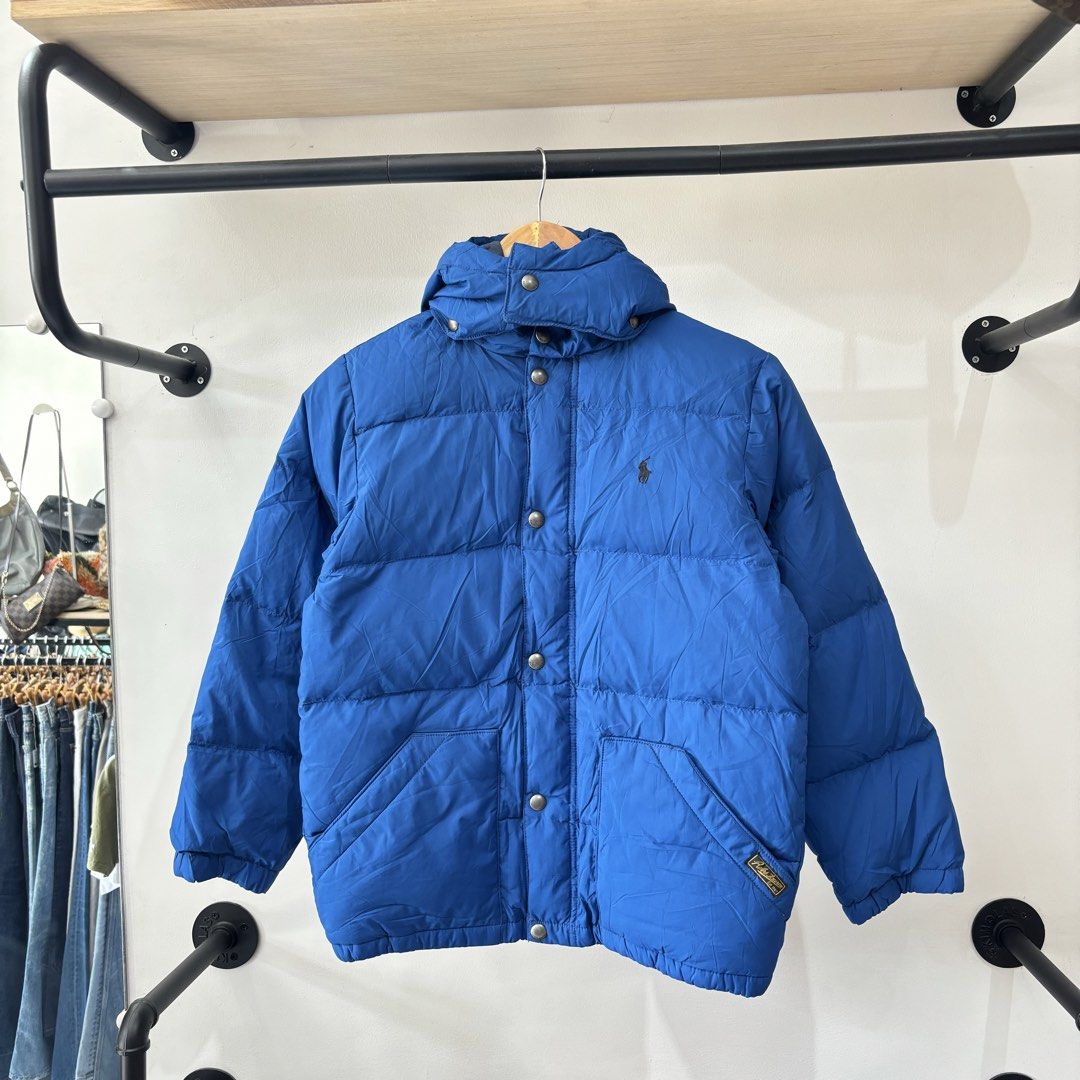 Polo Ralph Lauren Blue Puffer Jacket (Category: Coats, Jackets and Outerwear) located in Bambang. Submitted by heats777 (Listing ID 1471039454, Image 2). Description: - Brand: Polo Ralph Lauren - Color: Bright blue - Material: 100% polyester (quilted design for warmth) - Features: Attached hood, full zip with snap buttons, and two button-flap front pockets - Details: Iconic embroidered pony logo on the chest - Condition: Great outer layer for chi