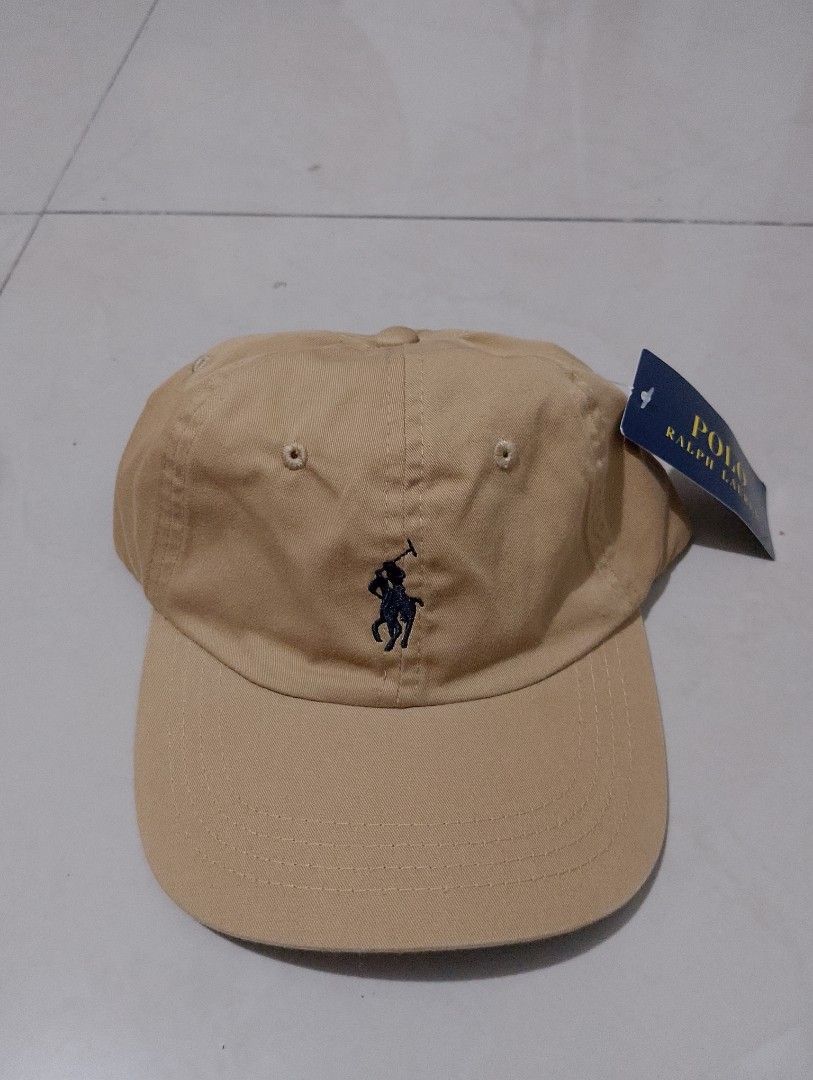 Polo Ralph Lauren Tan Baseball Cap (Category: Caps & Hats) located in Manila. Submitted by thriftyboyzzz (Listing ID 1470999134, Image 1). Description: - Brand: Polo Ralph Lauren - Color: Tan with dark navy embroidered polo player logo - Material: 100% cotton (Made in Bangladesh) - Design: Classic 6-panel with embroidered eyelets and curved brim - Fit: Adjustable strapback with metallic buckle (One size fits most) - Condition: Brand new with tags