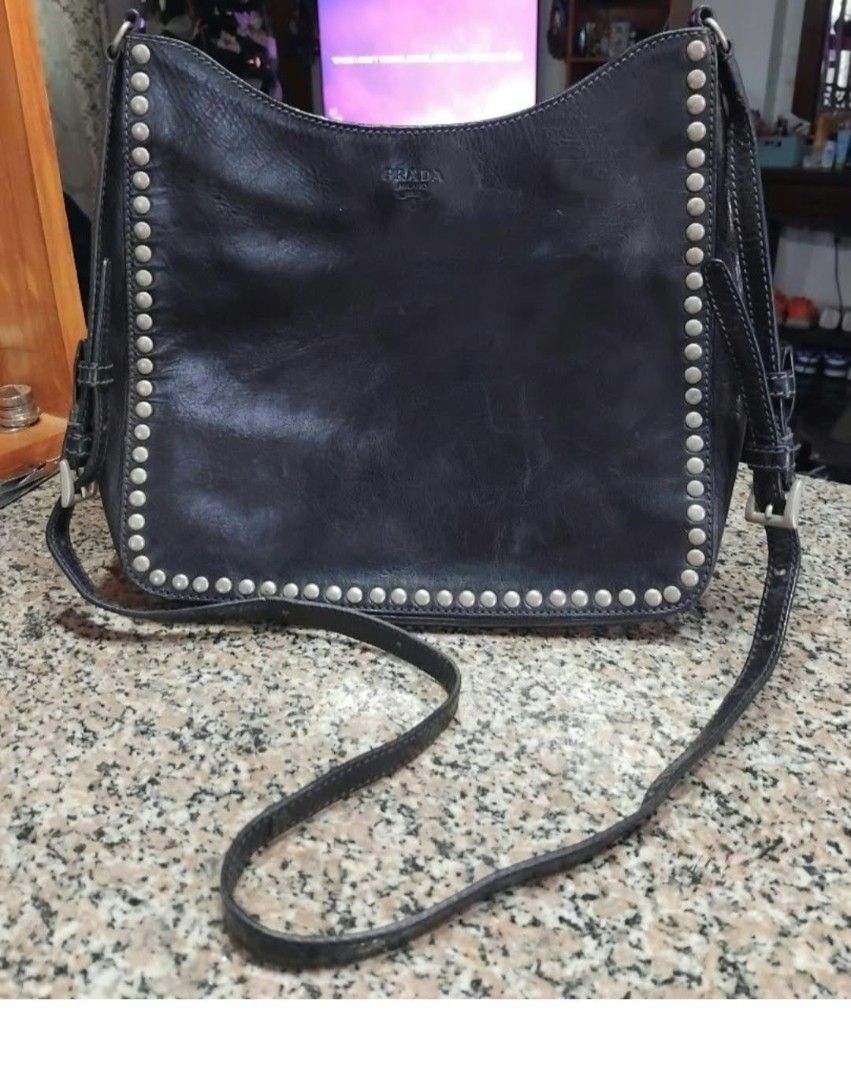 Prada Black Leather Studded Shoulder Bag (Category: Luxury Bags & Wallets) located in Lapu Lapu. Submitted by margaux099 (Listing ID 1471061986, Image 1). Description: - 100% Authentic Prada shoulder bag in classic black leather - Chic silver stud detailing along the edges and strap - Embossed Prada logo on the front - Secure zip top closure - Interior lined with signature Prada fabric - Includes an interior zippered pocket with metal tag and aut