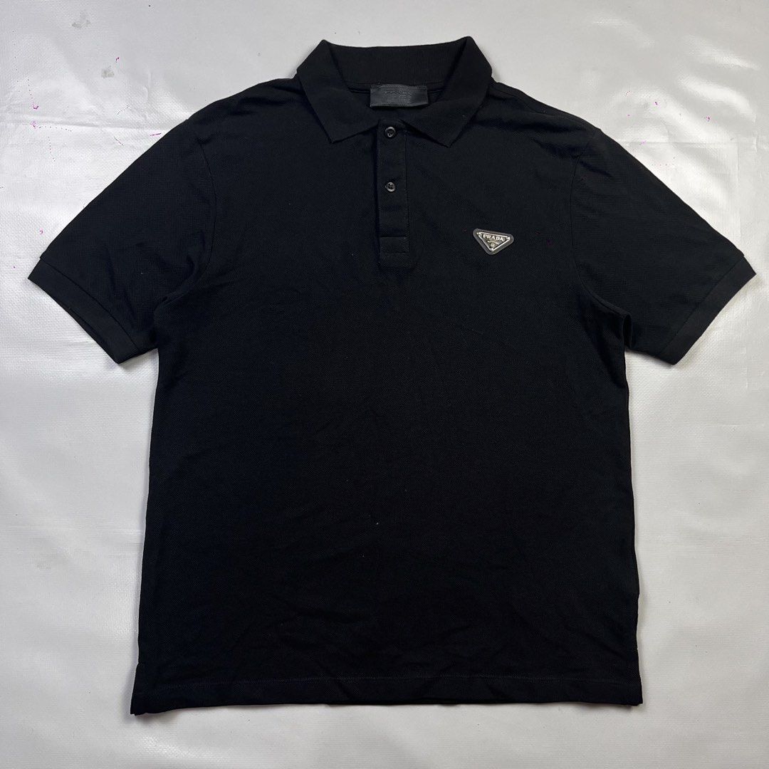 Prada Black Polo Shirt with Triangle Logo (Category: Tshirts & Polo Shirts ) located in Lucena. Submitted by nifty_finds (Listing ID 1470977122, Image 1). Description: Classic black Prada polo shirt in 100% cotton. Features the iconic metal and enamel triangle logo on the chest. Classic collar with a two-button placket. Made in Italy with standard care labels intact. Clean piece, great for casual wear..
