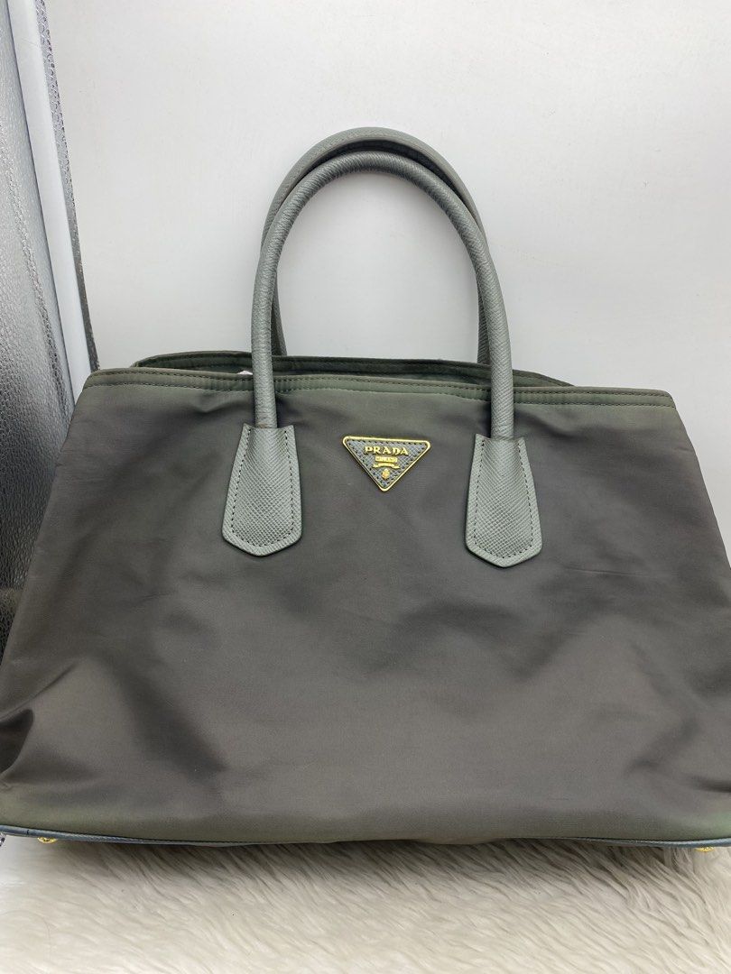 Prada Nylon Handbag Grey Tote Bag (Category: Luxury Bags & Wallets) located in Bacolod City. Submitted by chuchaystuffs (Listing ID 1470945228, Image 1). Description: - grey Prada tote bag - Durable nylon material with textured leather dual top handles - Iconic triangular logo plaque on the front - Elegant gold-tone hardware and structured base with protective metal feet - Spacious interior compartment, perfect for daily essentials - Comfortable 