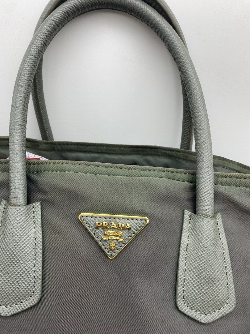 Prada Nylon Handbag Grey Tote Bag (Category: Luxury Bags & Wallets) located in Bacolod City. Submitted by chuchaystuffs (Listing ID 1470945228, Image 2). Description: - grey Prada tote bag - Durable nylon material with textured leather dual top handles - Iconic triangular logo plaque on the front - Elegant gold-tone hardware and structured base with protective metal feet - Spacious interior compartment, perfect for daily essentials - Comfortable 
