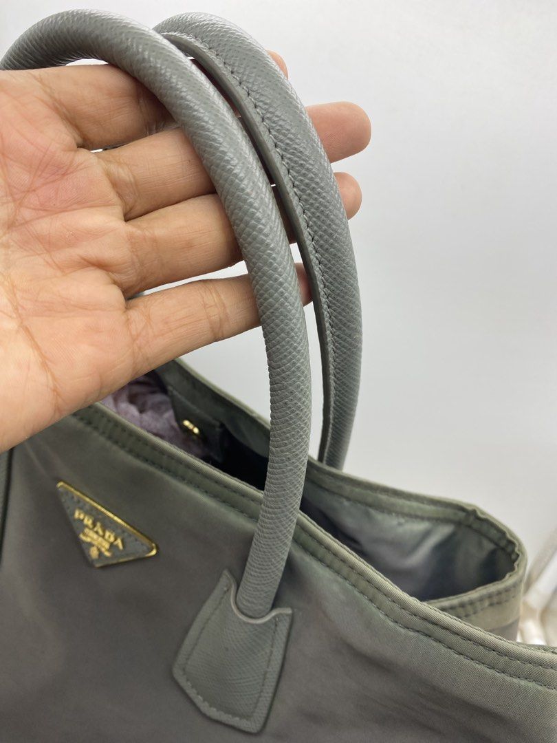 Prada Nylon Handbag Grey Tote Bag (Category: Luxury Bags & Wallets) located in Bacolod City. Submitted by chuchaystuffs (Listing ID 1470945228, Image 3). Description: - grey Prada tote bag - Durable nylon material with textured leather dual top handles - Iconic triangular logo plaque on the front - Elegant gold-tone hardware and structured base with protective metal feet - Spacious interior compartment, perfect for daily essentials - Comfortable 