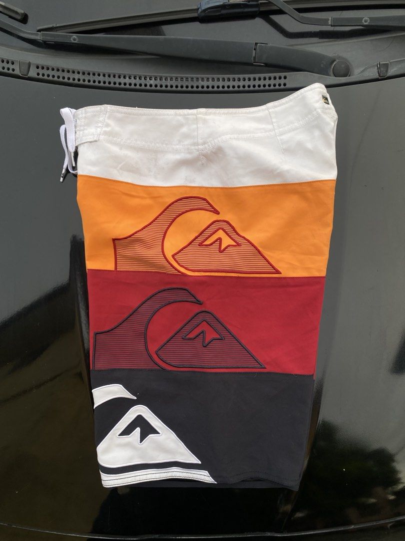 Quiksilver Colorblock Board Shorts Size 30 (Category: Swim Trunks & Board Shorts) located in Manila. Submitted by thriftmar (Listing ID 1471006537, Image 3). Description: - Brand: Quiksilver - Style Number: DOMBS332 - Size: 30 - Design: Multi-color panels (white, orange, red, black) with large vertical branding and mountain wave graphics - Features: Secure zip pocket on the right leg and lace-up drawstring closure at the waist - Condition: Excell