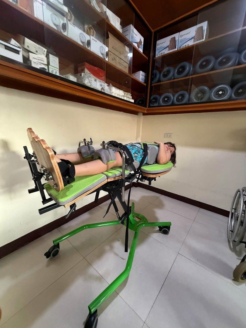 Rehatec pediatric standing frame green and grey (Category: Medical Supplies & Tools) located in Manila. Submitted by calmdolphin.87b0e4 (Listing ID 1470957310, Image 2). Description: - Pediatric therapeutic standing frame with green and grey padding - Includes headrest, secure torso straps, and adjustable knee blocks - Wooden footplates equipped with foot straps for stability - Mounted on a mobile wheeled base for easy repositioning - Features bu