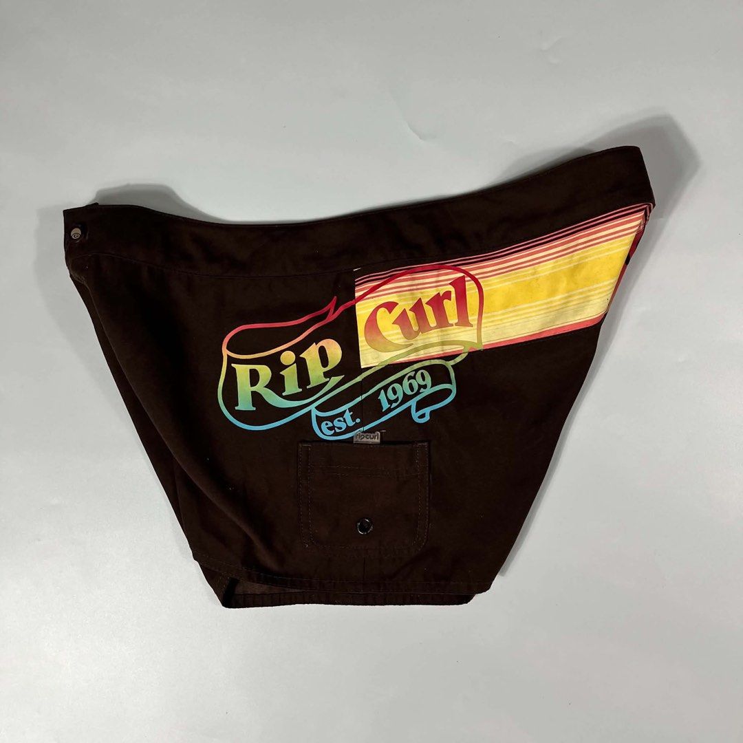 Rip Curl Retro Sun Print Board Shorts Brown (Category: Swim Trunks & Board Shorts) located in Iloilo. Submitted by dripnest.ilo (Listing ID 1471098905, Image 3). Description: - Brand: Rip Curl - Color/Design: Brown with colorful retro stripes and sun graphics - Special Feature: Side cargo pocket with attached wax comb - Details: Vibrant rainbow fading on logo and back panel, yellow-lined waistband - Closure: Button fly - Style: Classic surf aesth