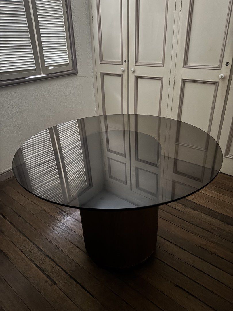 Round Smoke Glass Dining Table with Fluted Wood Base (Category: Tables & Sets) located in Makati City. Submitted by maria.1024 (Listing ID 1471117463, Image 1). Description: Modern round dining table with a smoked-glass tabletop and an elegant cylindrical pedestal base featuring vertical fluted detailing in a bronze-brown finish. Dimensions: * Glass tabletop diameter: 42 inches * Pedestal base diameter: 19 inches * Overall height: 28 inches Condi