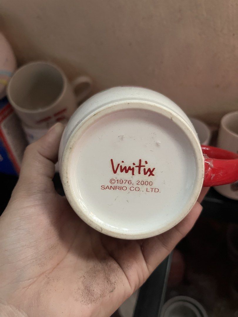 Sanrio Vivitix Hello Kitty Mushroom Ceramic Mug (Category: Coffee & Tea Tableware) located in Manila. Submitted by janetecson05 (Listing ID 1471118166, Image 2). Description: - Authentic Sanrio Vivitix Kitty ceramic mug (Dated 1976, 2000 Sanrio Co., Ltd.) - Features Kitty in a pink outfit surrounded by cute mushrooms and grass - Eye-catching bright red handle and standard mug size - Storage find with minor dust/spots, just needs a quick wash befo