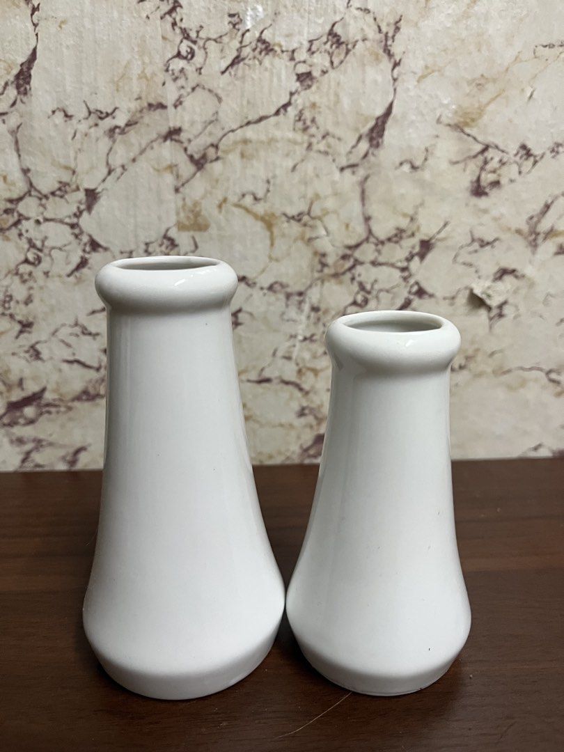Set of two white ceramic bud vases (Category: Vases & Decorative Bowls) located in Manila. Submitted by kayerrr.gem (Listing ID 1471046929, Image 1). Description: - Set of 2 white ceramic vases in varying heights - Minimalist modern style with flared bases and rounded rims - Smooth, glossy glaze finish - Ideal for single stems or small floral arrangements - Neutral tone complements any home decor - Condition: Bottoms show minor wear and discolora