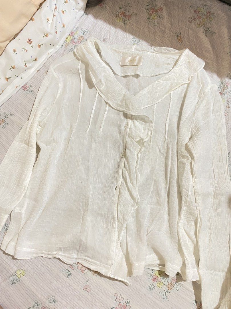Simida White Ruffle Collar Button-Down Blouse (Category: Blouses) located in Imus. Submitted by softclosetph (Listing ID 1471108473, Image 1). Description: - Brand: Simida - Color: White - Style: Long sleeves, button-front closure - Details: Soft ruffle collar, textured crinkle fabric - Fit/Material: Lightweight, easy to pair with skirts or pants - Condition: Clean and well-maintained.