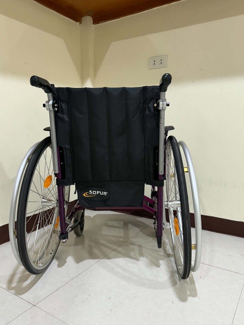 Sopur Purple Wheelchair Folding Mobility Aid (Category: Wheelchairs) located in Manila. Submitted by calmdolphin.87b0e4 (Listing ID 1470959947, Image 3). Description: - Brand: Sopur - Color: Vibrant purple frame with black upholstery - Portability: Foldable design for easy transport and storage - Mobility: Large rear wire wheels with handrims and reflectors, plus smooth front caster wheels - Comfort: Padded armrests and supportive backrest - Supp