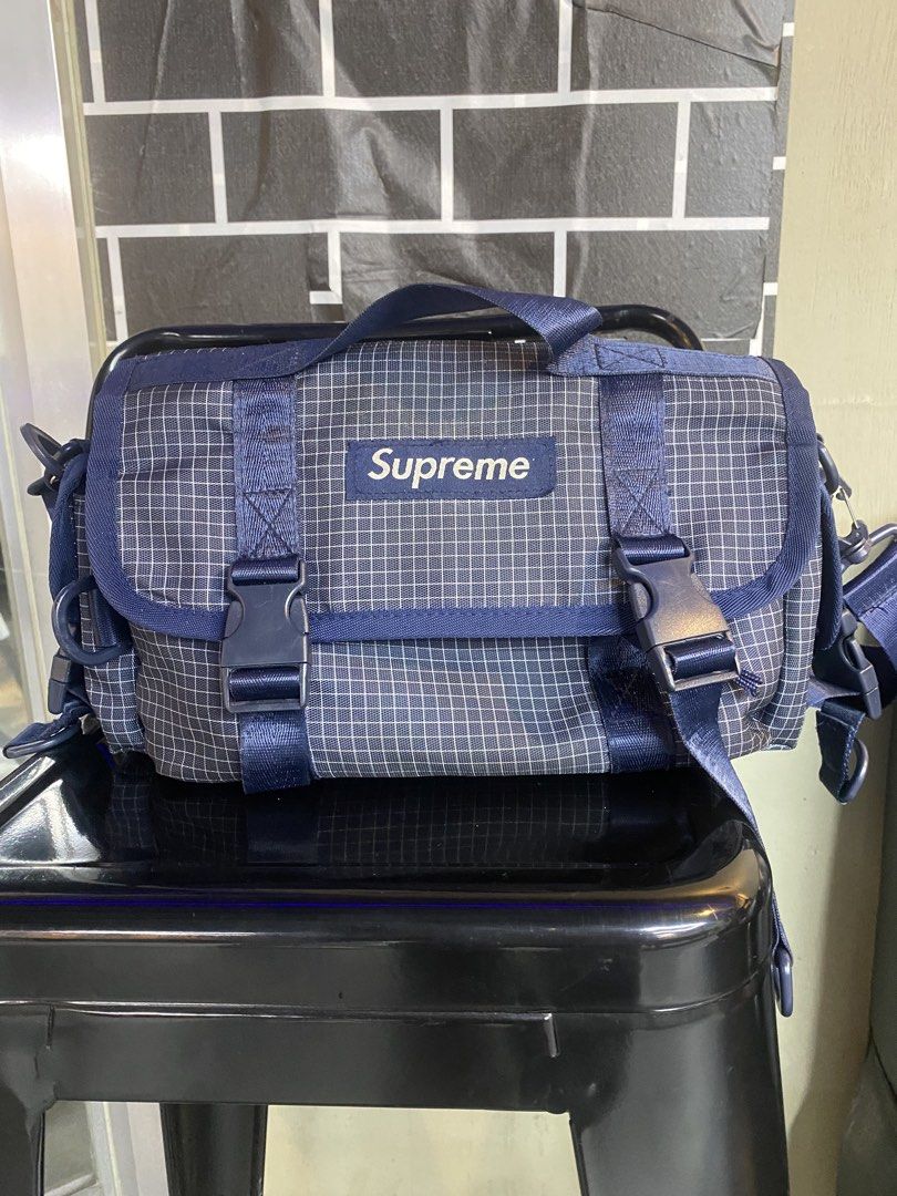 Supreme Grid Pattern Messenger Bag Blue (Category: Sling Bags) located in Manila. Submitted by lancee1208 (Listing ID 1471039069, Image 1). Description: Supreme messenger bag in dark blue grid pattern fabric. Dual buckle closure on the front flap with brand logo patch. Top handle and adjustable shoulder strap with padded grip. Spacious main compartment inside, zippered pocket, and inner dividers. Clean black lining throughout. Sturdy hardware and