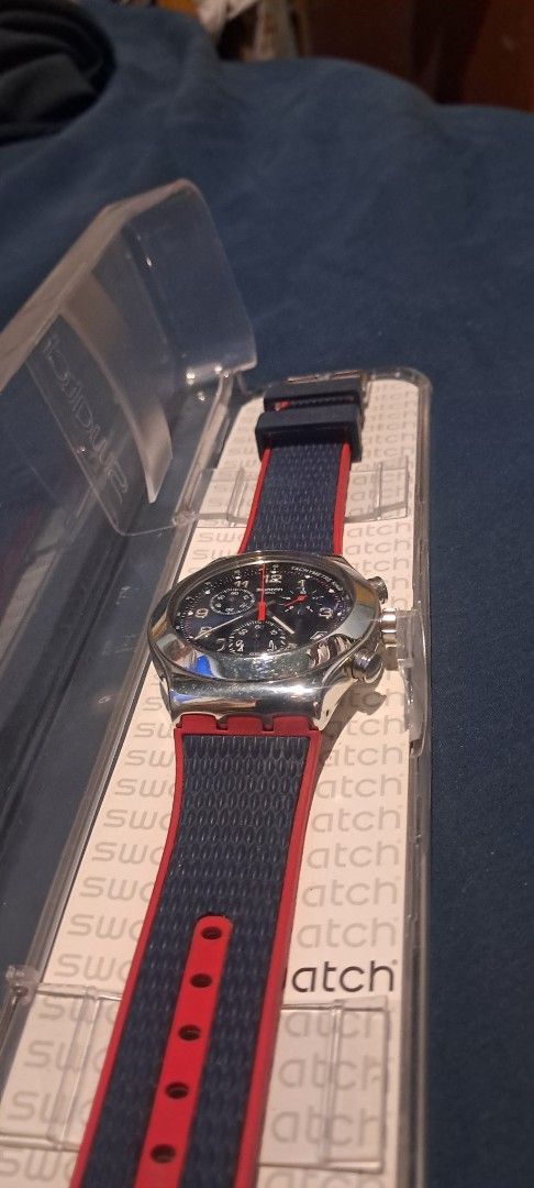 Swatch Chrono Watch Blue Red Strap with Original Case (Category: Men's Watches) located in Calaca. Submitted by ramirdollosocastro (Listing ID 1471020588, Image 2). Description: - Brand: Swatch Chronograph - Dial: Blue dial with date window near 4 o'clock - Bezel: Tachymeter scale - Strap: Red and navy blue textured strap with secure buckle closure - Inclusion: Original clear plastic storage case - Condition: Excellent / Ready to wear.