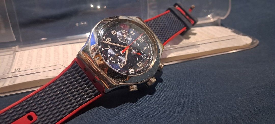 Swatch Chrono Watch Blue Red Strap with Original Case (Category: Men's Watches) located in Calaca. Submitted by ramirdollosocastro (Listing ID 1471020588, Image 3). Description: - Brand: Swatch Chronograph - Dial: Blue dial with date window near 4 o'clock - Bezel: Tachymeter scale - Strap: Red and navy blue textured strap with secure buckle closure - Inclusion: Original clear plastic storage case - Condition: Excellent / Ready to wear.
