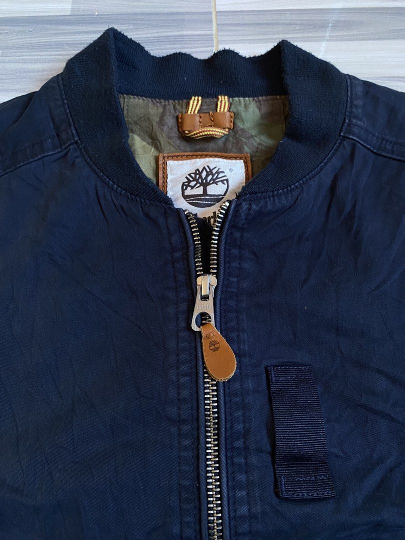 Timberland Navy Bomber Jacket with Camo Lining (Category: Coats, Jackets and Outerwear) located in Bayambang. Submitted by vintagestuffph (Listing ID 1471066242, Image 3). Description: - Brand: Timberland - Color: Classic Navy Blue - Style: Bomber jacket with full zip closure and leather zipper pull - Details: Ribbed collar, cuffs, and hem; round leather Timberland logo patch on left sleeve - Pockets: Two front welt pockets and a utility chest po