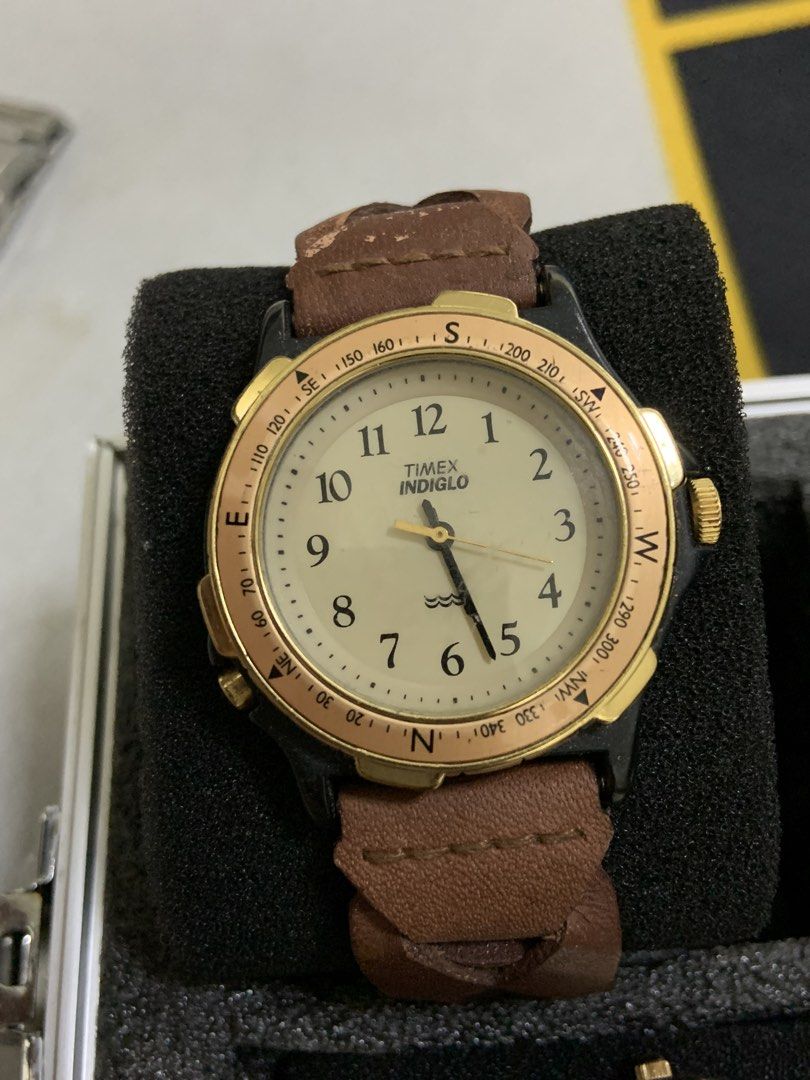 Timex Indiglo Compass Leather Strap Watch (Category: Men's Watches) located in Manila. Submitted by relokado (Listing ID 1470938503, Image 1). Description: - Brand: Timex Indiglo - Dial: Cream dial with dark numerals and water resistance symbol - Bezel: Gold-tone compass bezel with directional markings and degree scales - Case: Dark case with multiple side pushers - Strap: Brown leather strap (note: shows visible wear and cracking near the top lu