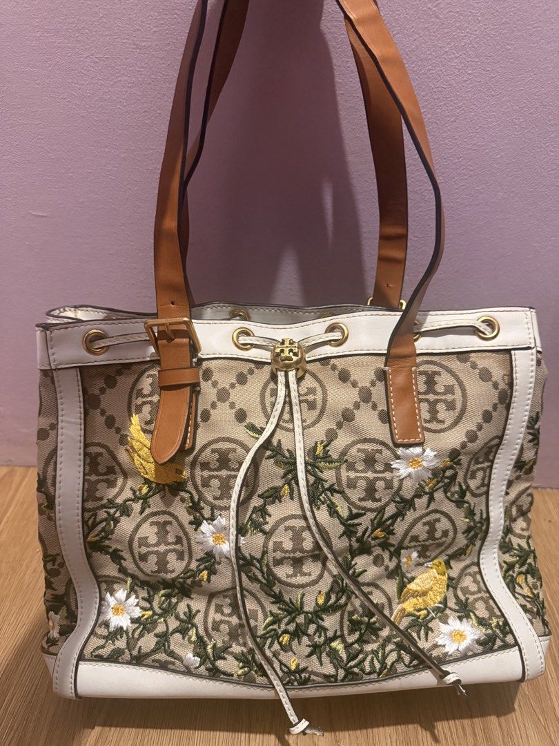 Tory Burch Monogram Embroidered Tote Bag (Category: Tote Bags) located in Pasig City. Submitted by sea321 (Listing ID 1470941735, Image 1). Description: - Brand: Tory Burch - Material: Beige monogram canvas with brown & white leather trim - Design: Colorful embroidered birds and floral vine details on the front - Hardware: Gold-tone hardware with protective metal feet on the base - Closure: Drawstring closure - Interior: Tan lining with a zippere