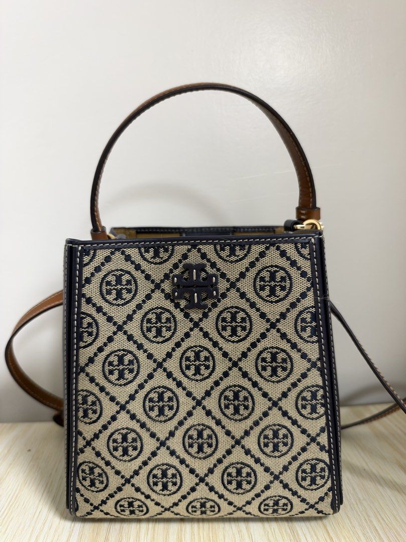Tory Burch Monogram Jacquard Small Bucket Bag (Category: Luxury Bags & Wallets) located in Manila. Submitted by cat-d526 (Listing ID 1470984098, Image 1). Description: - Brand: Tory Burch - Design: Navy and cream diamond monogram canvas with dark navy leather side panels and white contrast stitching - Hardware: Gold-tone - Straps: Brown top handle and adjustable crossbody strap - Closure: Open top with internal magnetic tab strap - Interior: Neut