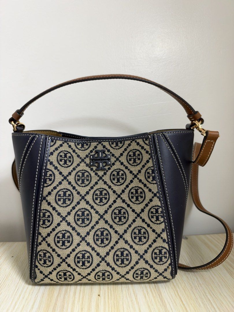Tory Burch Monogram Jacquard Small Bucket Bag (Category: Luxury Bags & Wallets) located in Manila. Submitted by cat-d526 (Listing ID 1470984098, Image 2). Description: - Brand: Tory Burch - Design: Navy and cream diamond monogram canvas with dark navy leather side panels and white contrast stitching - Hardware: Gold-tone - Straps: Brown top handle and adjustable crossbody strap - Closure: Open top with internal magnetic tab strap - Interior: Neut