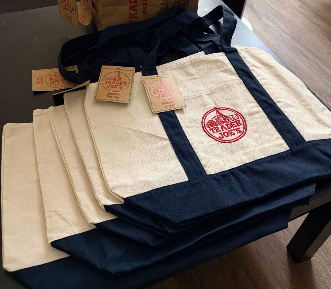 Trader Joe's Canvas Tote Bag (Category: Tote Bags) located in Tabaco. Submitted by goodiestuffs86 (Listing ID 1471038842, Image 1). Description: - Brand: Trader Joe's - Style: Reusable canvas tote bag (Navy Blue & Cream) - Condition: Brand new with original paper tags attached - Material: Thick, durable cotton fabric with sturdy dark blue straps and bottom panel - Features: Front pocket with embroidered red logo, spacious interior - Perfect for: 