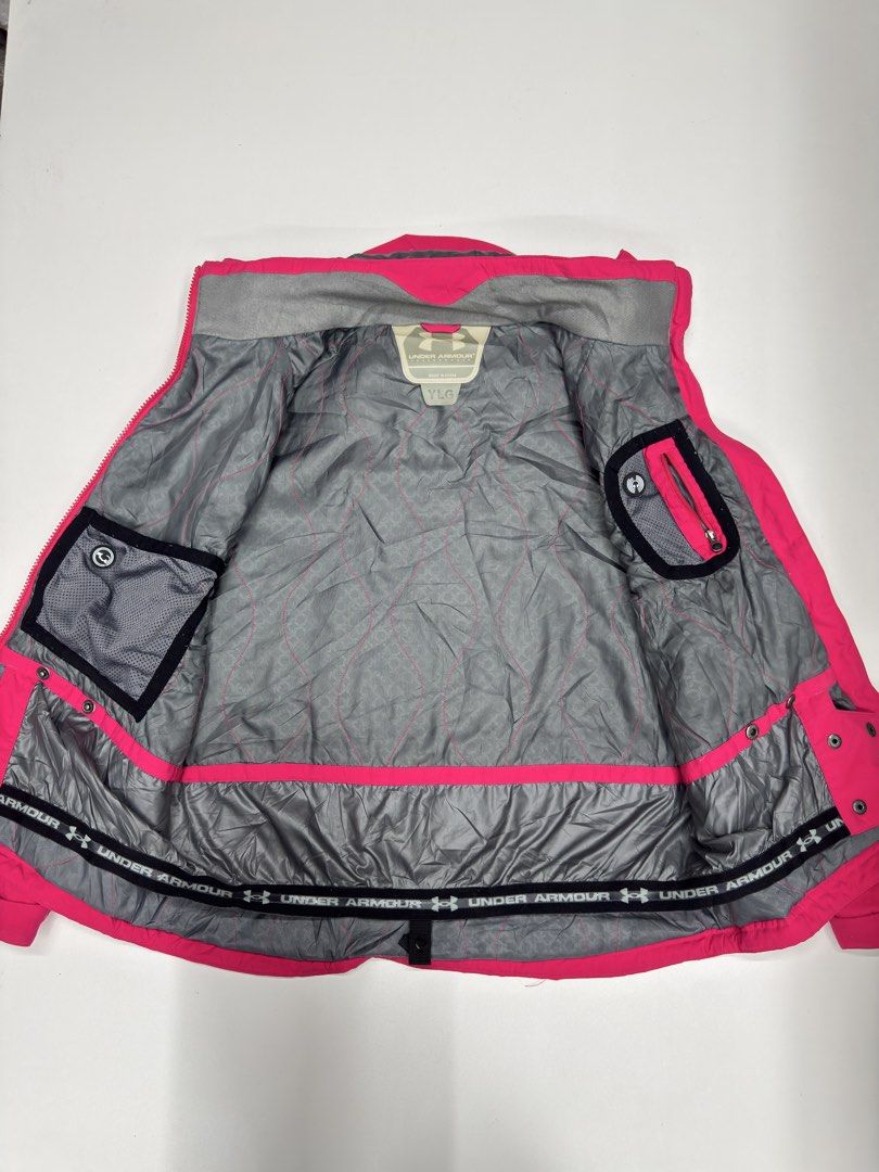 Under Armour Pink Youth Large Winter Jacket Coat (Category: Coats, Jackets and Outerwear) located in Bustos. Submitted by thenlnclot60500 (Listing ID 1470936140, Image 2). Description: - Brand: Under Armour - Size: Youth Large - Color: Bright pink with white logos on chest and back - Lining: Grey quilted with hexagonal pattern - Closure: Zip-up front with snap button storm flap - Features: Attached hood, multiple interior pockets, and elastic pow