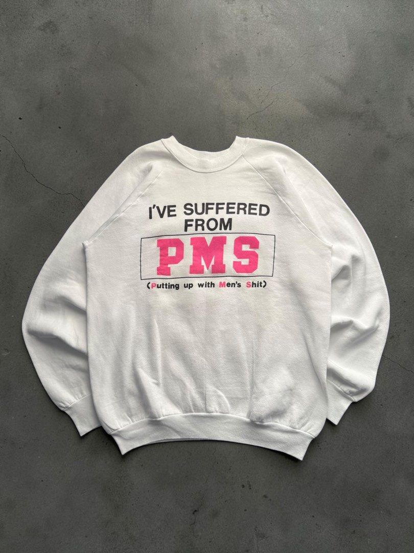 Vintage 1990’s PMS Humor Statement Sweater (Category: Coats, Jackets and Outerwear) located in Pasig City. Submitted by hoardwrld (Listing ID 1470989774, Image 1). Description: Width: 23 Length: 28 - Style: White crewneck sweatshirt with raglan sleeves - Design: Bold 'I'VE SUFFERED FROM PMS (Putting up with Men's Shit)' graphic print on chest - Size & Material: XL, 50% cotton and 50% polyester blend - Comfort: Cozy interior fleece lining - Condit