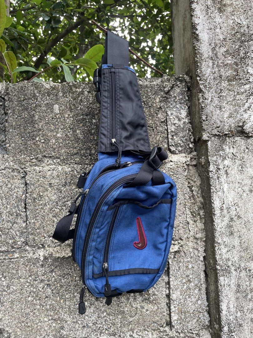 Vintage Nike Blue Crossbody Sling Bag (Category: Sling Bags) located in Cebu City. Submitted by lucky.finds.ph (Listing ID 1470972793, Image 2). Description: - Color: Royal blue body with black straps and hardware - Brand: Nike with branded Woojin Duraflex buckle - Design: Distinct raised red and brown Nike swoosh on the front zippered pocket - Storage: Multiple compartments including an additional zip compartment on the main strap for daily carr
