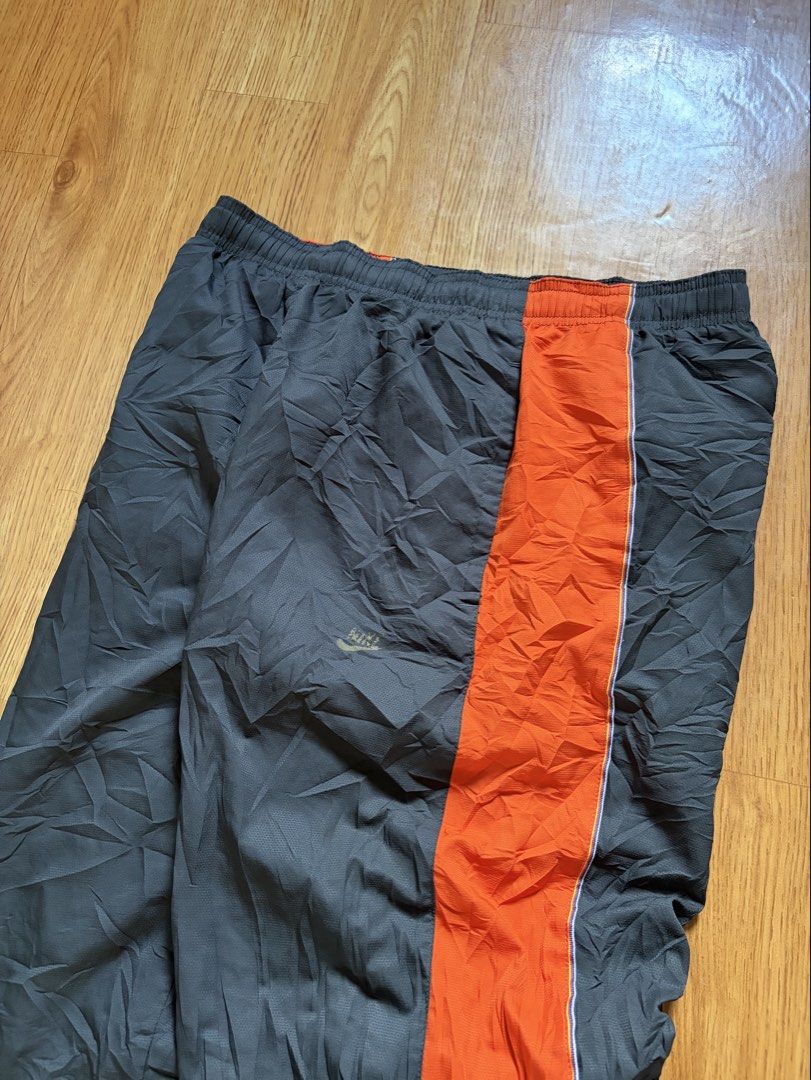 Vintage Nike Track Pants Dark Grey Orange (Category: Joggers) located in Angeles City. Submitted by repurposedwear (Listing ID 1471116163, Image 2). Description: Vintage Nike track pants in dark grey and orange. Size L / US 34. Features lightweight nylon material, a rare rainbow woven tag, adjustable elastic drawstring waist, and bottom side zips with ankle toggle cinch cords. Great vintage condition. Issues : nike logo on the thigh is faded, als