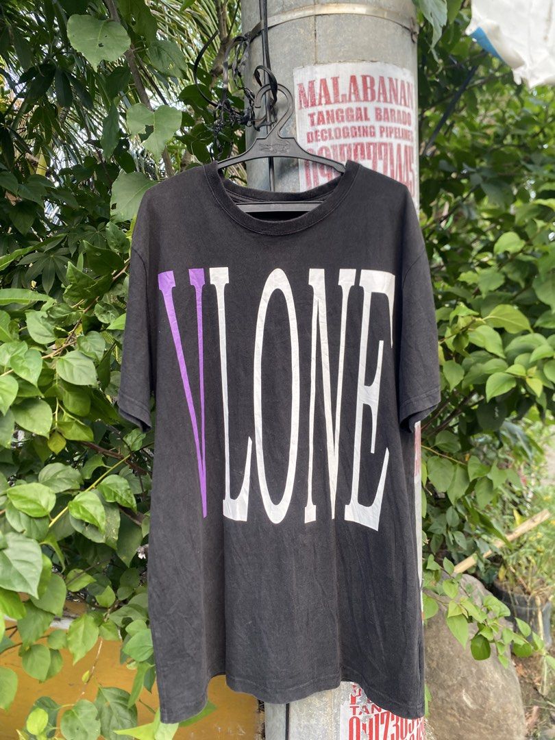 Vlone Black Purple Tee Shirt (Category: Tshirts & Polo Shirts ) located in Lucena. Submitted by puffinthrift (Listing ID 1470988452, Image 1). Description: - Color: Black - Design: Large graphic text on front with signature purple 'V' on the chest, and large purple 'V' print on the back - Fit: Relaxed fit with short sleeves and classic crew neck - Material: Comfortable, high-quality cotton fabric - Style: Versatile streetwear piece, easy to match